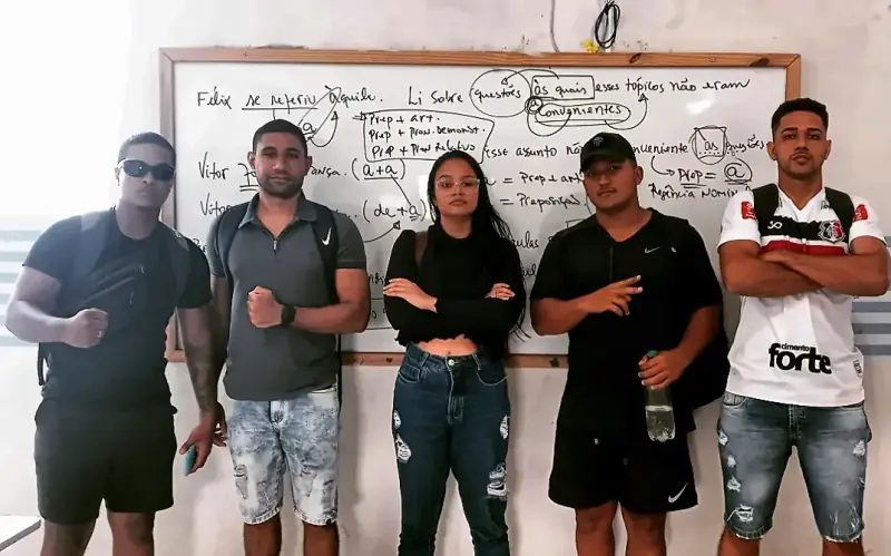 Cinco alunos em pé diante do quadro branco com anotações de aula